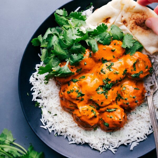 Plate with butter chicken meatballs served on a bed of rice, garnished with fresh cilantro, with naan bread on the side.