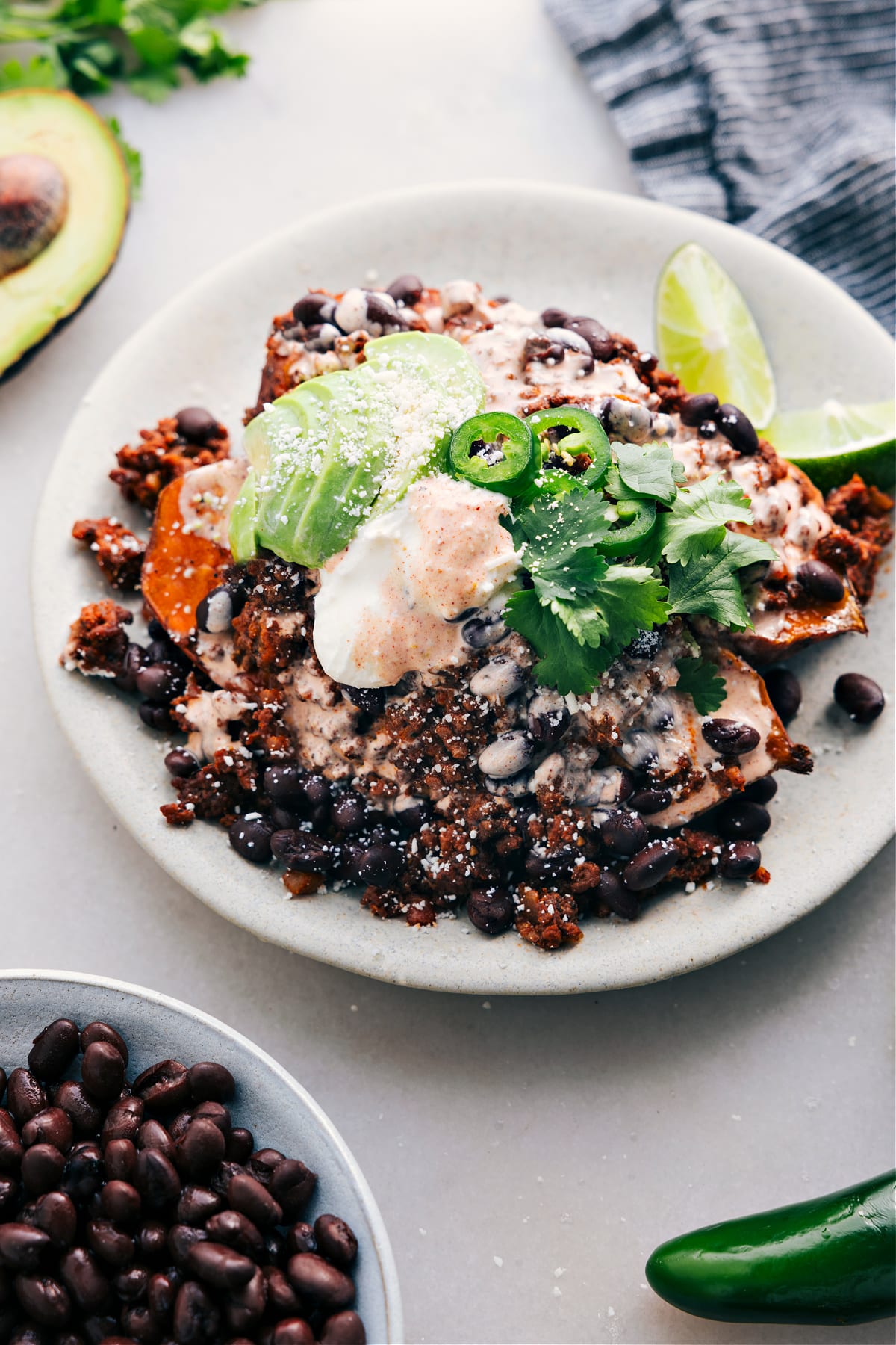 Taco Stuffed Sweet Potatoes are served on a plate and loaded with meat, avocado, sauce, jalapeño, and fresh cilantro.