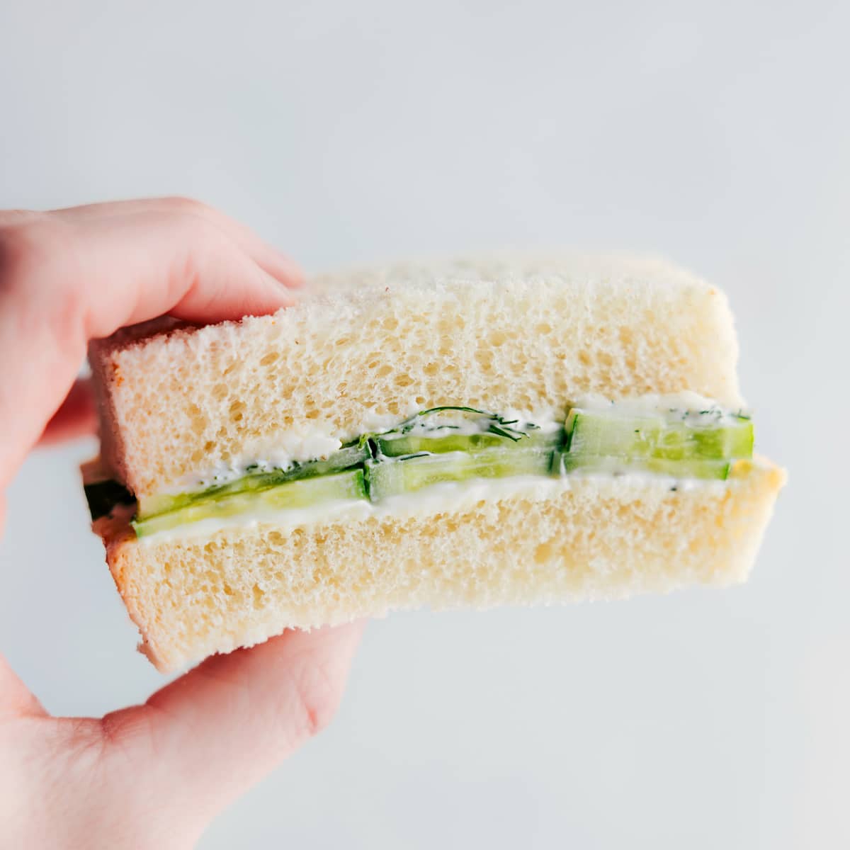 A cucumber sandwich being held up showing the yummy insides.