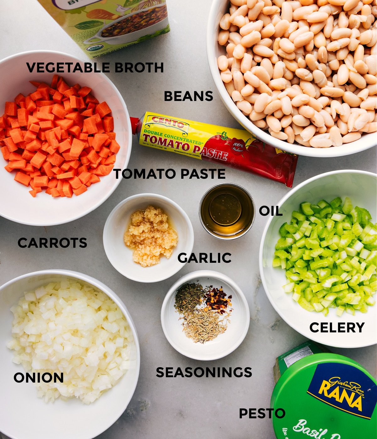 All the ingredients for this recipe are prepped and ready for easy assembly, including broth, beans, paste, oil, garlic, veggies, seasonings, and pesto.