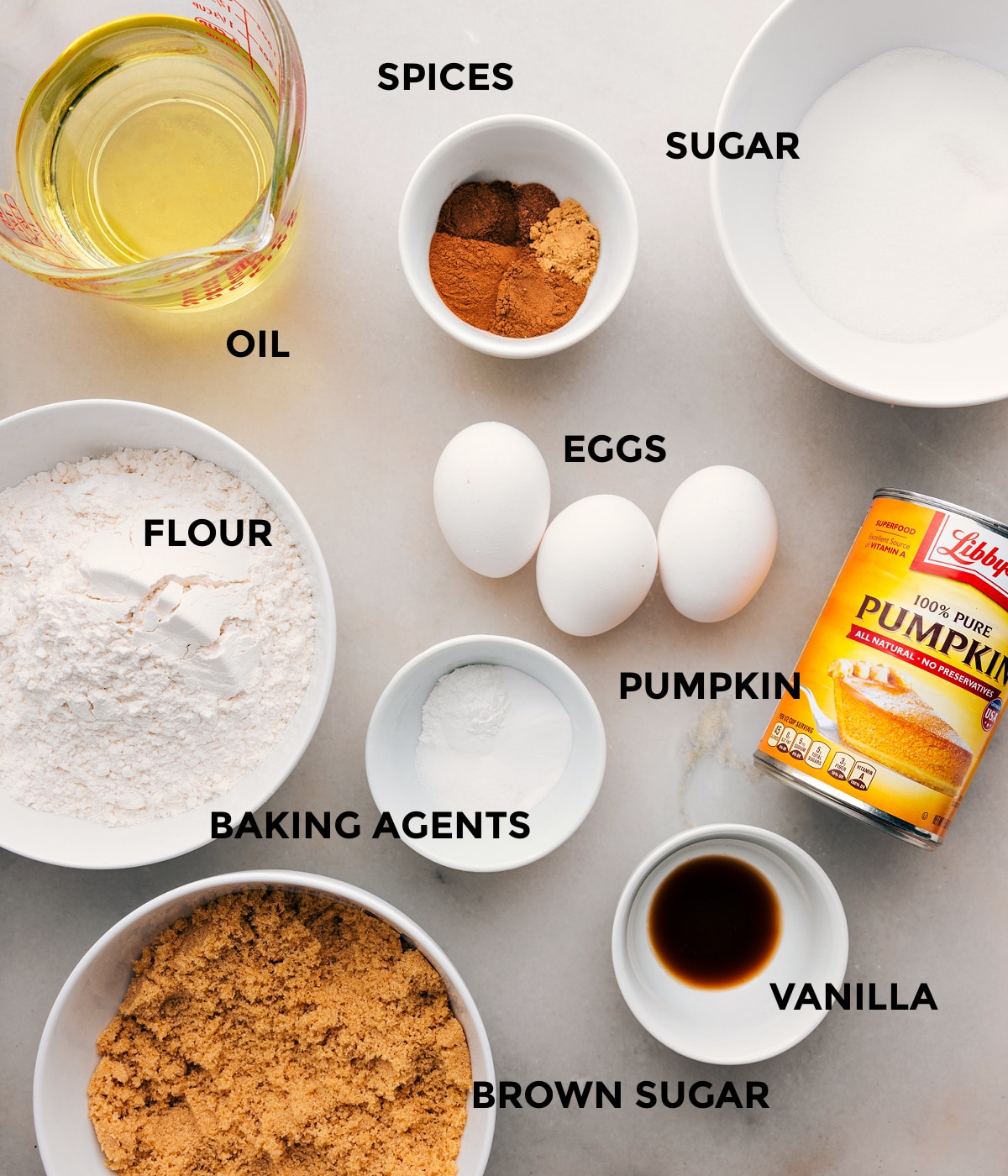 All the ingredients in this recipe including oil, sugar, spices, eggs, flour, baking agents, and pumpkin prepped out for easy assembly.