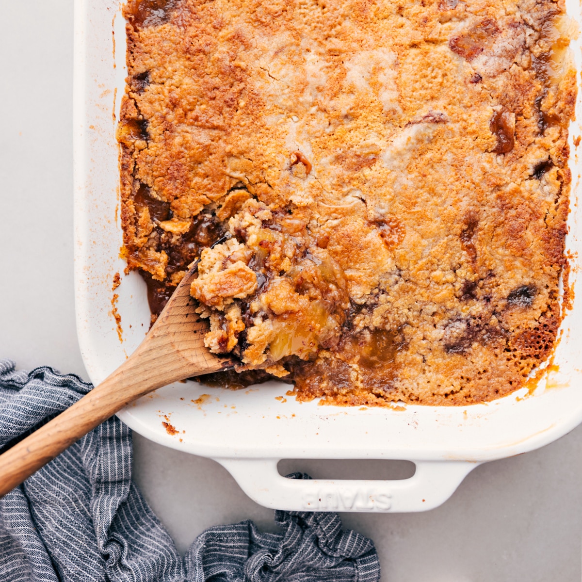 Apple dump cake in the casserole with a spoon taking out a scoop.