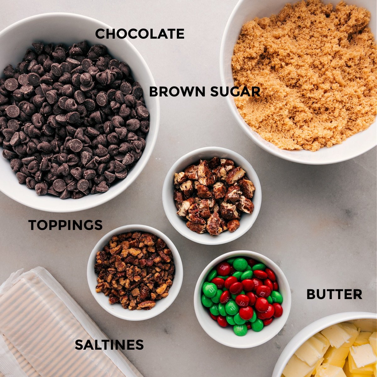 The ingredients for this recipe are prepped for easy assembly: chocolate, brown sugar, toppings, butter, and saltines.