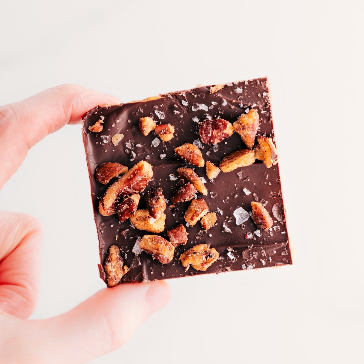 A Christmas Crack square is held up, topped with candied pecans.