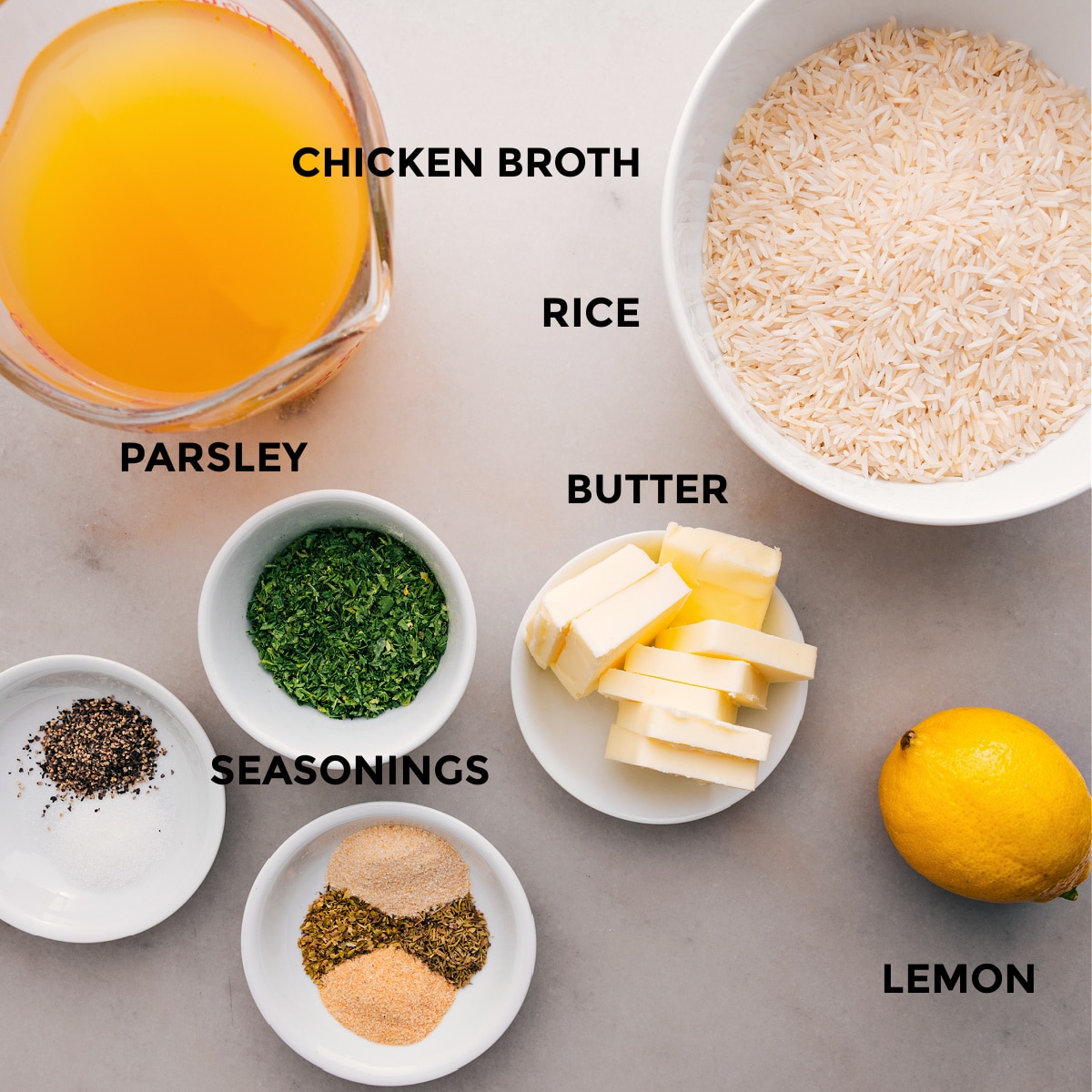 All the ingredients for this recipe are prepped for easy assembly: chicken broth, seasonings, butter, rice, lemon, and fresh parsley.