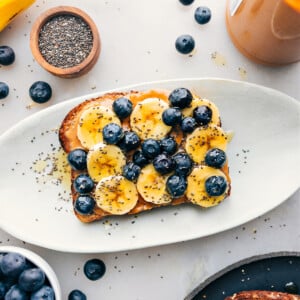 Breakfast toast on a platter with all the fun toppings like bananas, blueberries, chia seeds, and honey.