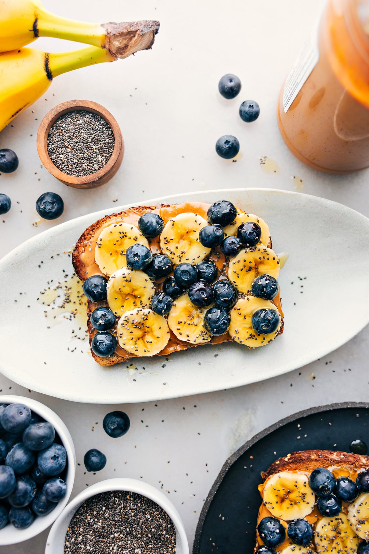 Breakfast toast on a platter with all the fun toppings like bananas, blueberries, chia seeds, and honey.