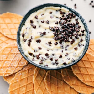 The best Cannoli Dip in a bowl with waffle crackers ready to be dipped in.