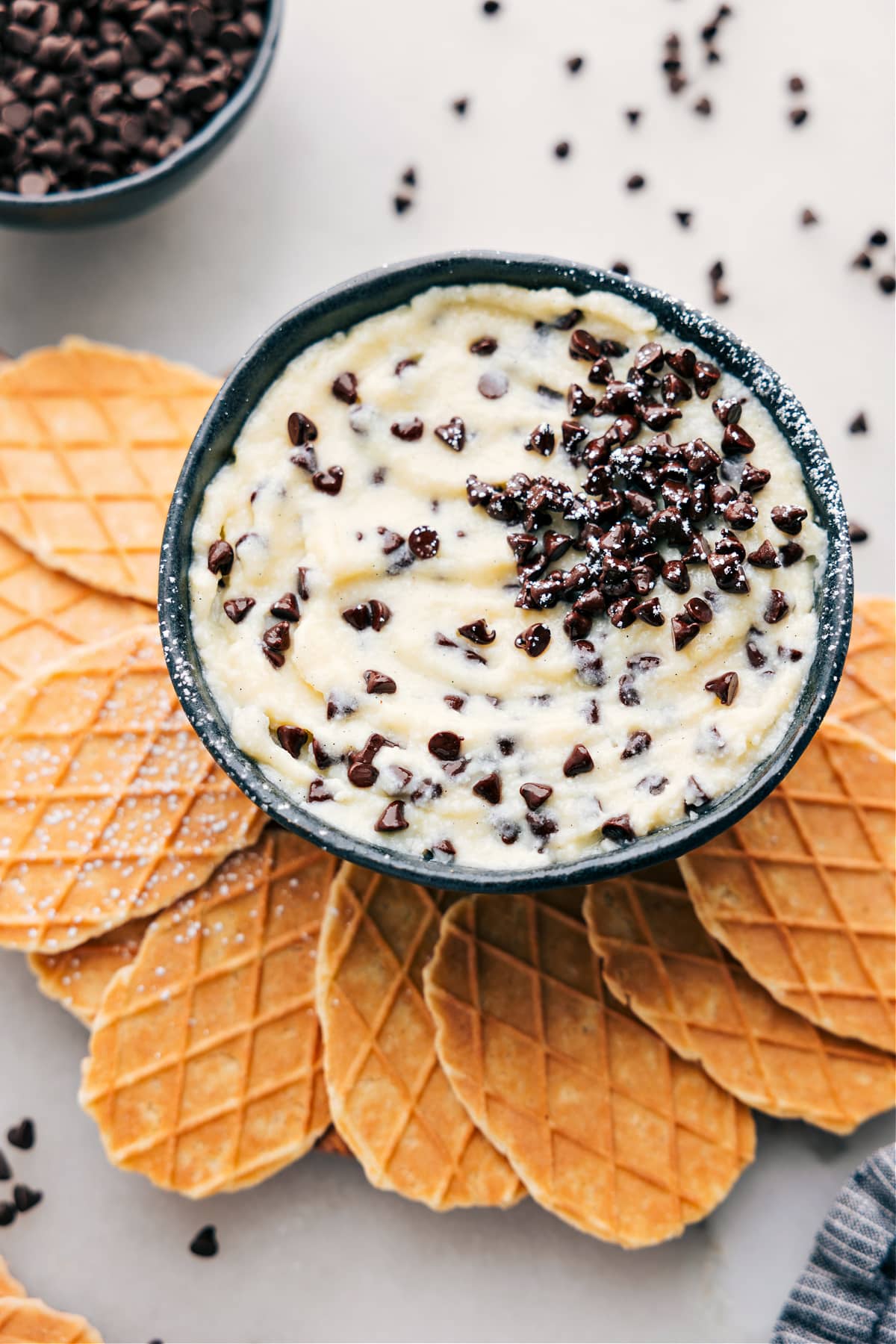 The best Cannoli Dip in a bowl with waffle crackers ready to be dipped in.