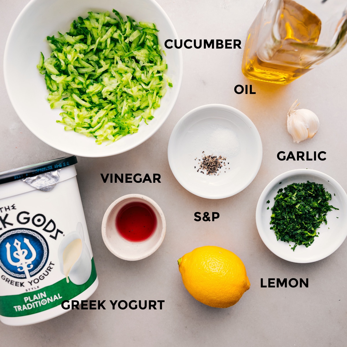 All the ingredients are prepped for easy assembly, including oil, cucumbers, yogurt, vinegar, garlic, herbs, salt, and pepper.