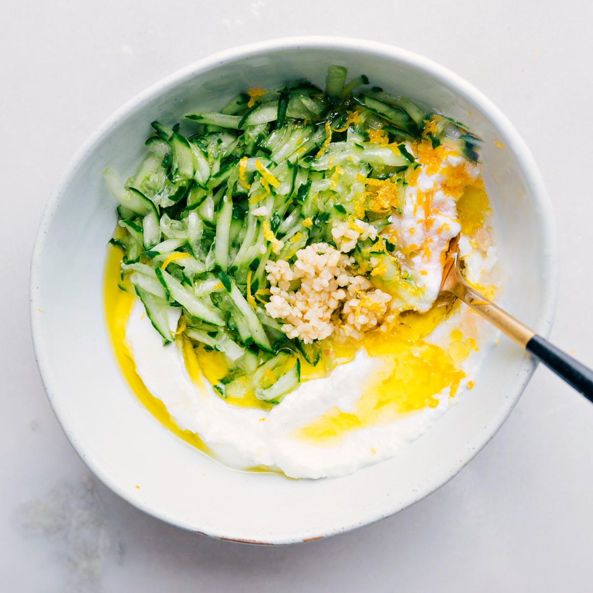 Adding all the tzatziki sauce ingredients to a bowl and whisking them together.