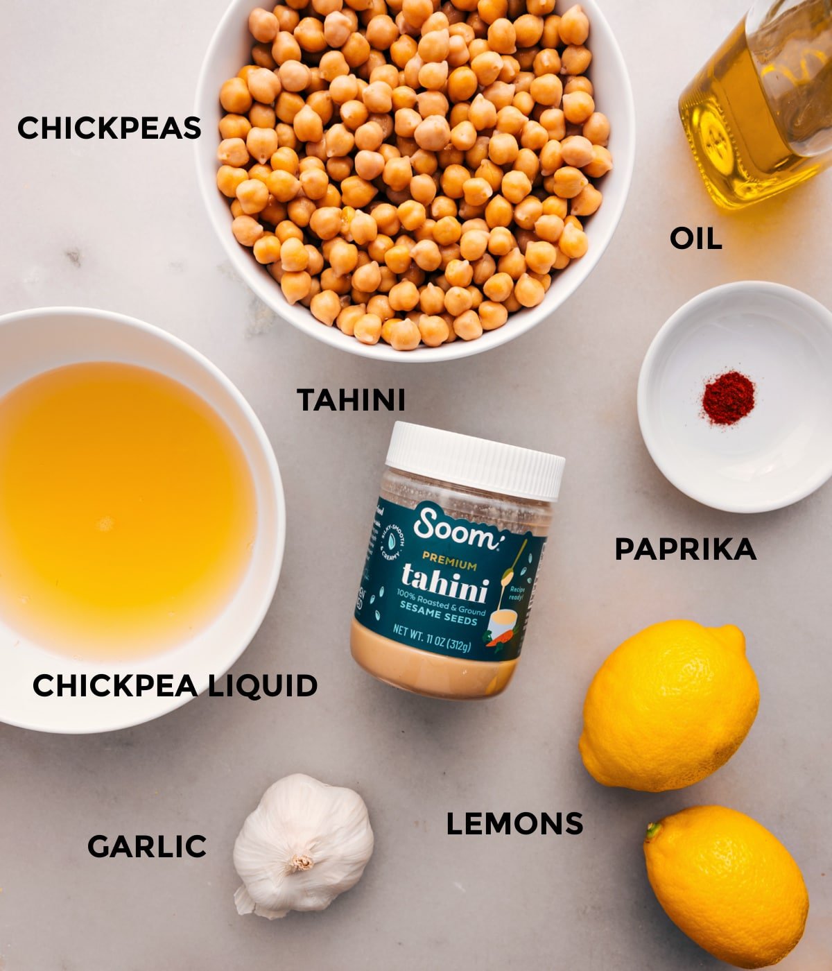 All the ingredients prepped for easy assembly, including oil, chickpeas, tahini, paprika, lemons, and garlic.