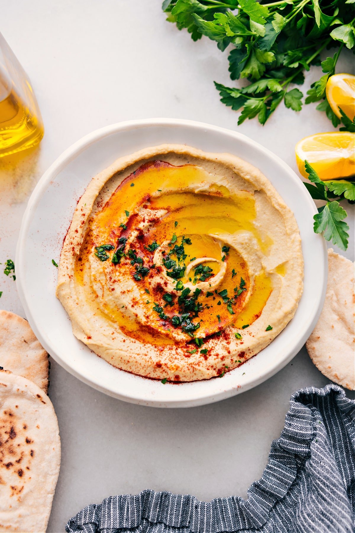 Hummus in a bowl with fresh olive oil, herbs, and paprika on top.