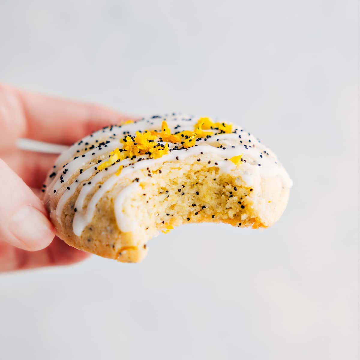 The treat with a glaze and fresh lemon zest on top with a bite out of it.