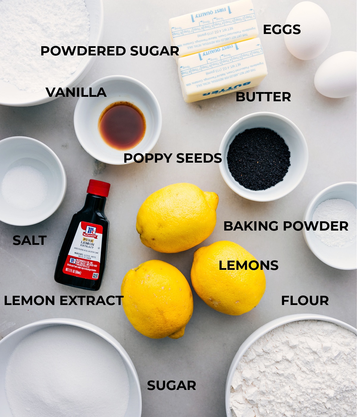 All the ingredients in this recipe are prepped and ready for easy assembly: eggs, powdered sugar, vanilla, poppy seeds, baking powder, lemons, lemon extract, and salt.