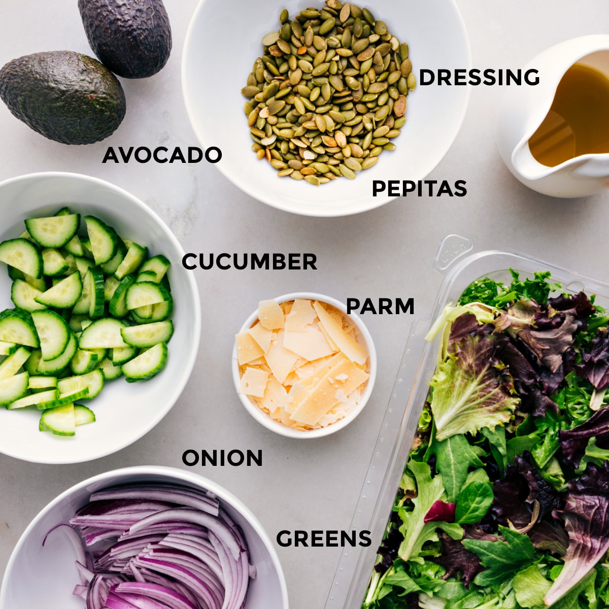 All the ingredients for this recipe—dressing, pepitas, avocado, cucumber, parm, greens, and onion—prepped and ready for easy assembly.