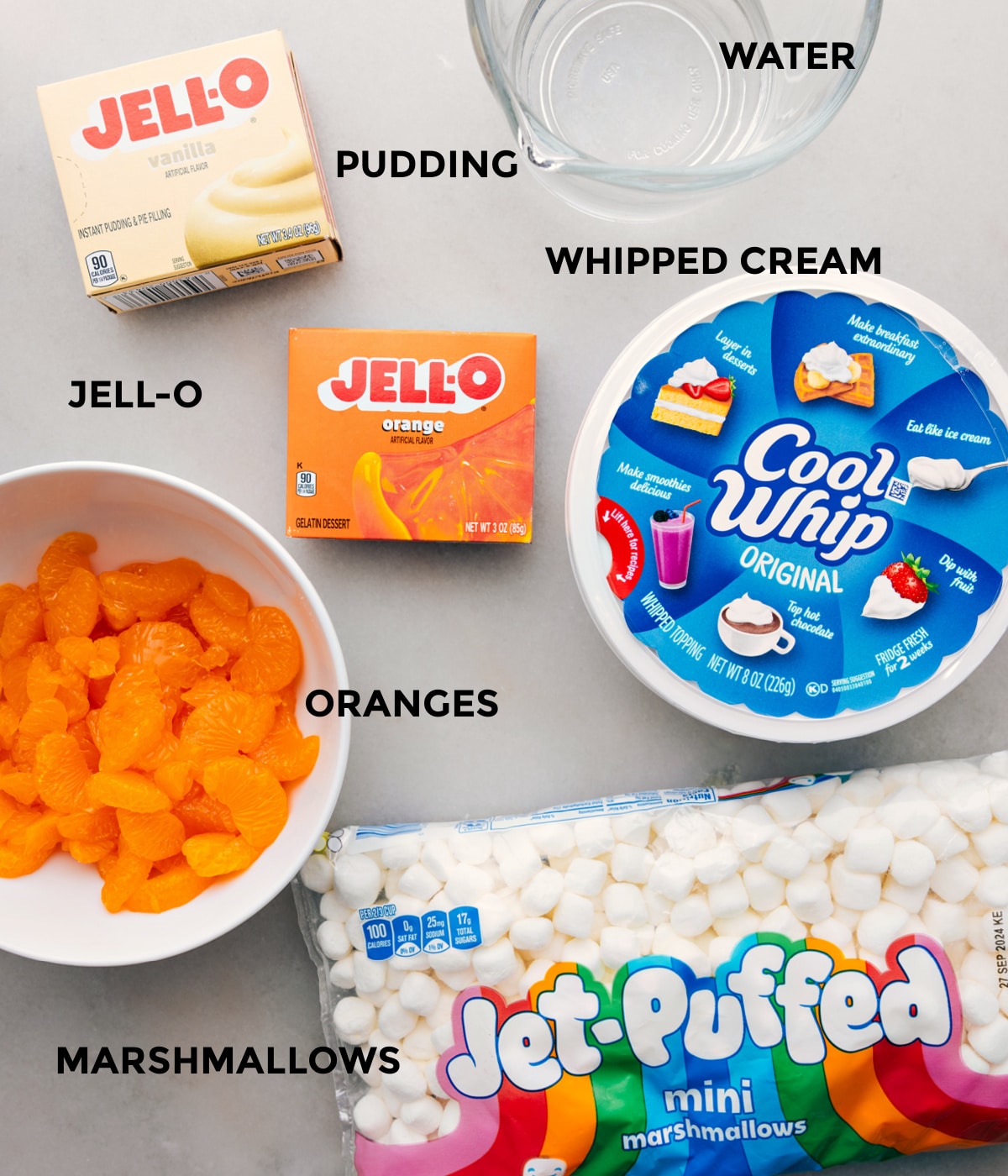 All the ingredients for this recipe including mandarins, jell-o, cool whip, and mini marshmallows prepped out for easy assembly.