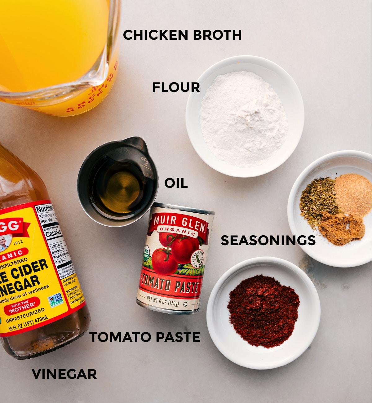 All the ingredients for this recipe are prepped and ready for easy assembly, including chicken broth, flour, seasonings, oil, tomato paste, and apple cider vinegar.