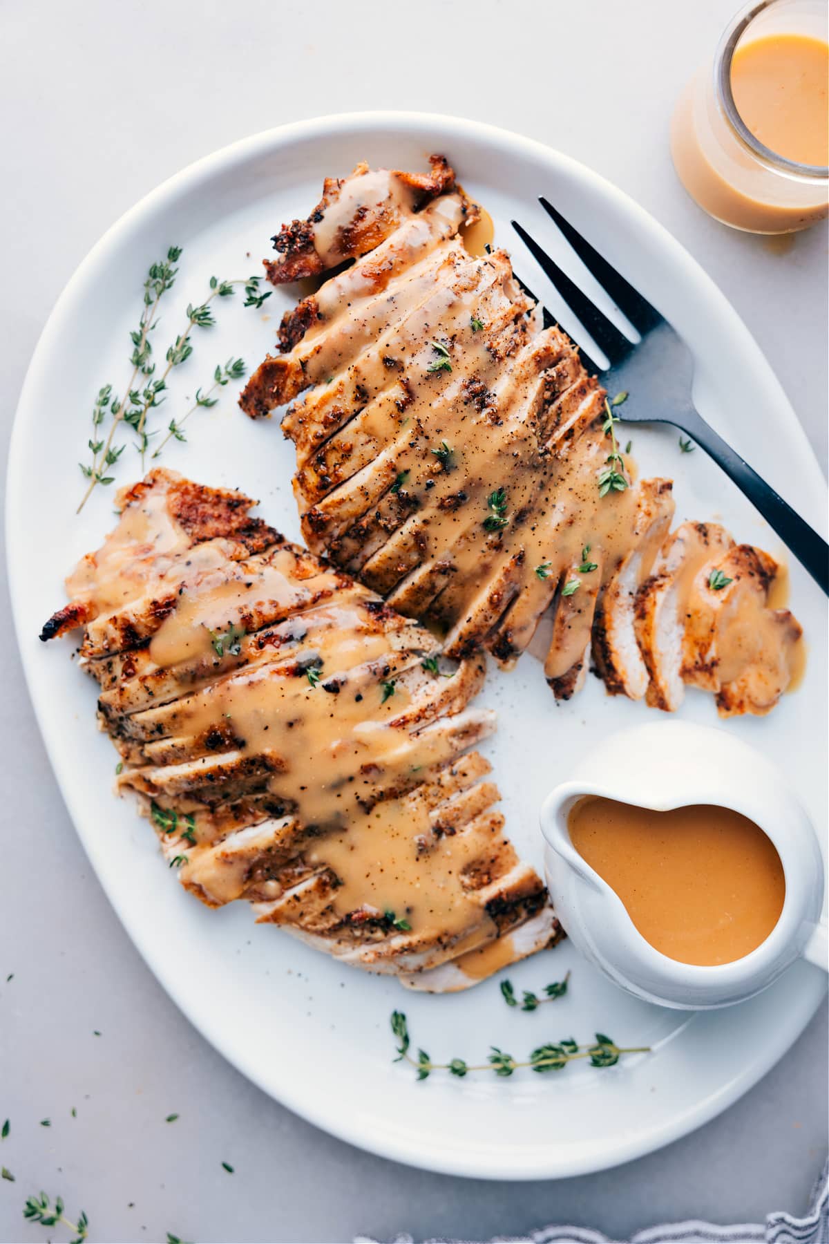 Sliced turkey breast cooked in a crockpot, served on a plate topped with gravy and garnished with fresh herbs.