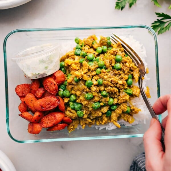 A meal-prepped tupperware container filled with rice, savory Indian ground turkey, roasted vegetables, and sauce, ready for a quick and delicious meal.