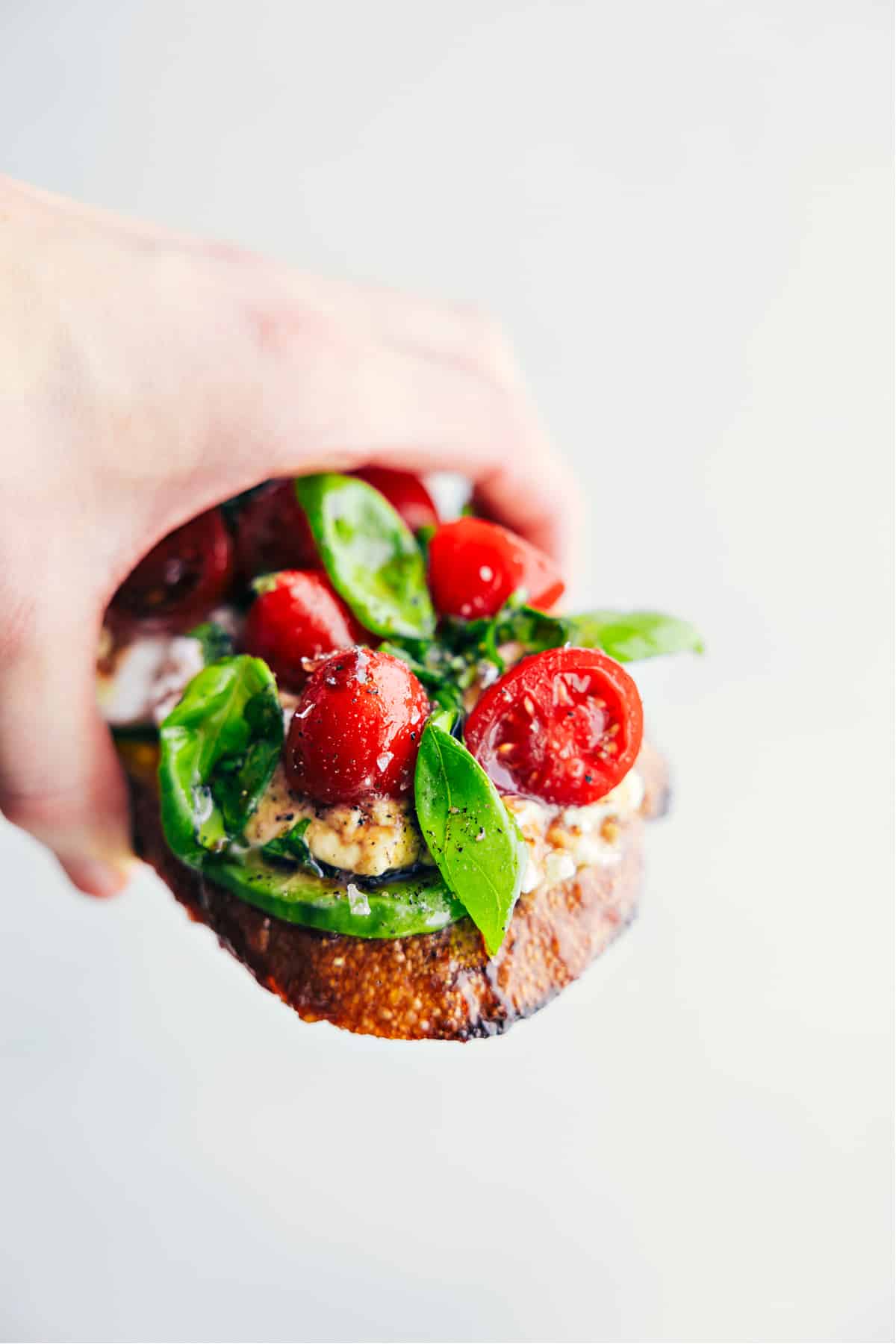 A piece of cottage cheese toast being held up showing all the yummy toppings.