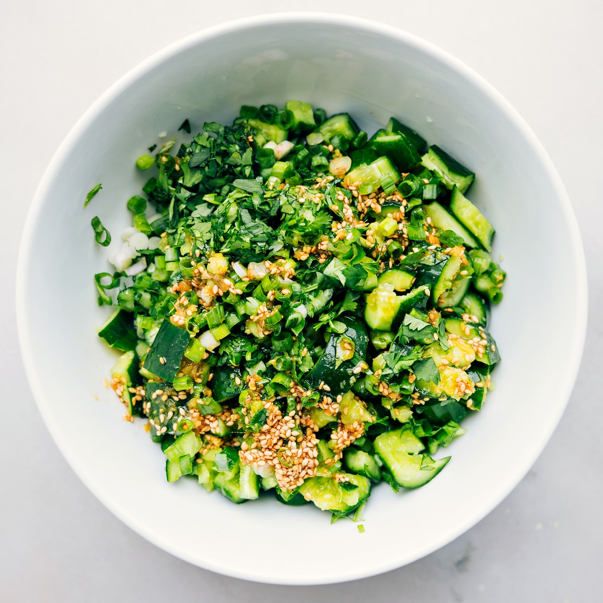 Smashed Cucumber Salad in a bowl with dressing and herbs ready to be tossed together