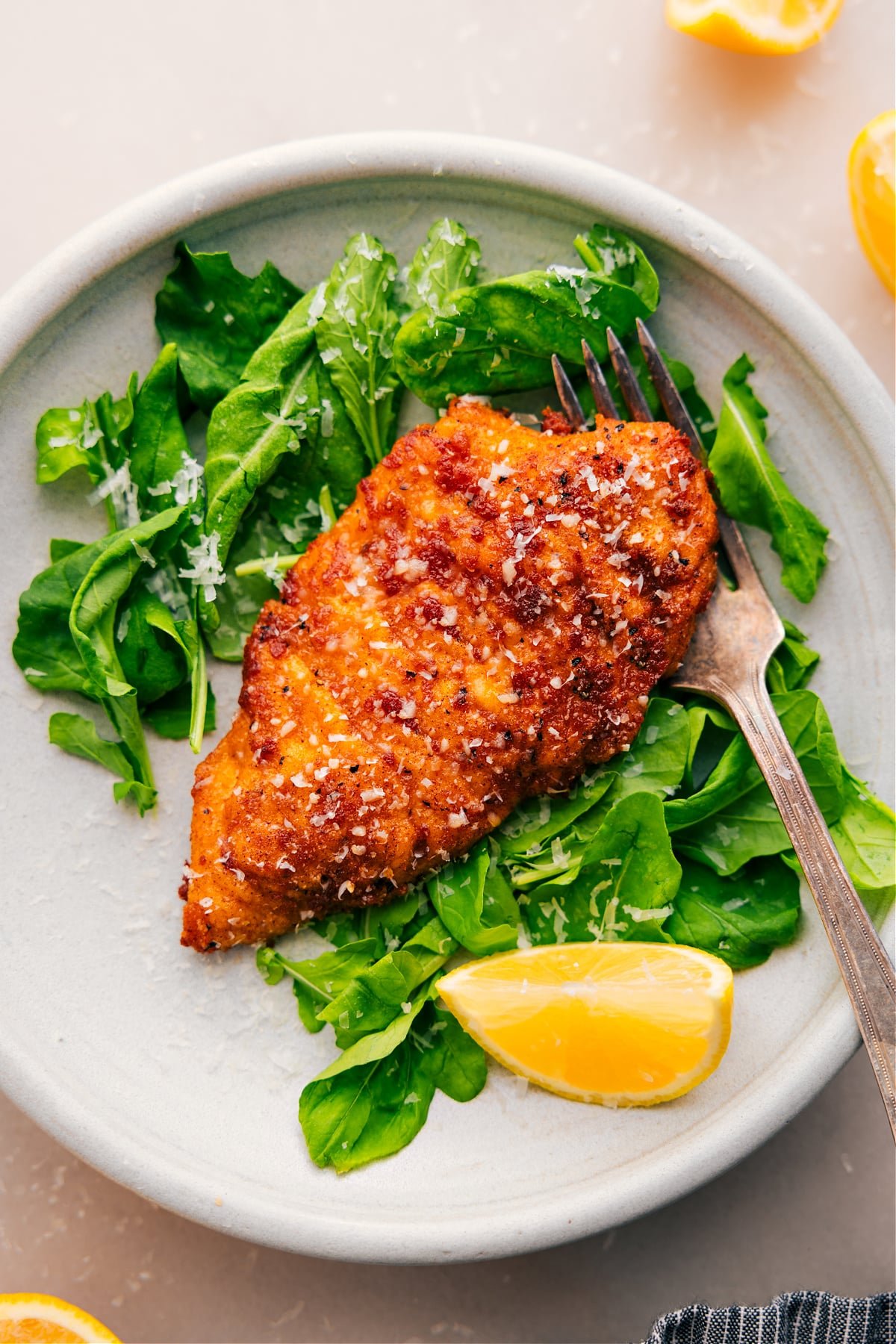 Crispy and delicious Chicken Cutlets rest on a bed of greens with a squeeze of lemon on the side.