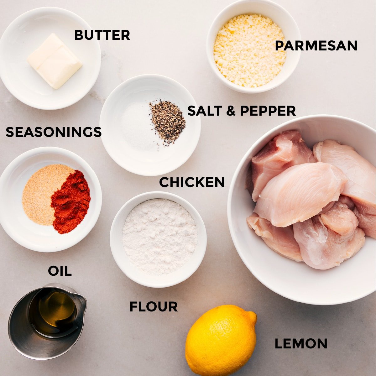 All the ingredients for this recipe are prepped and ready for easy assembly: butter, parmesan, seasonings, meat, flour, lemon, and oil.