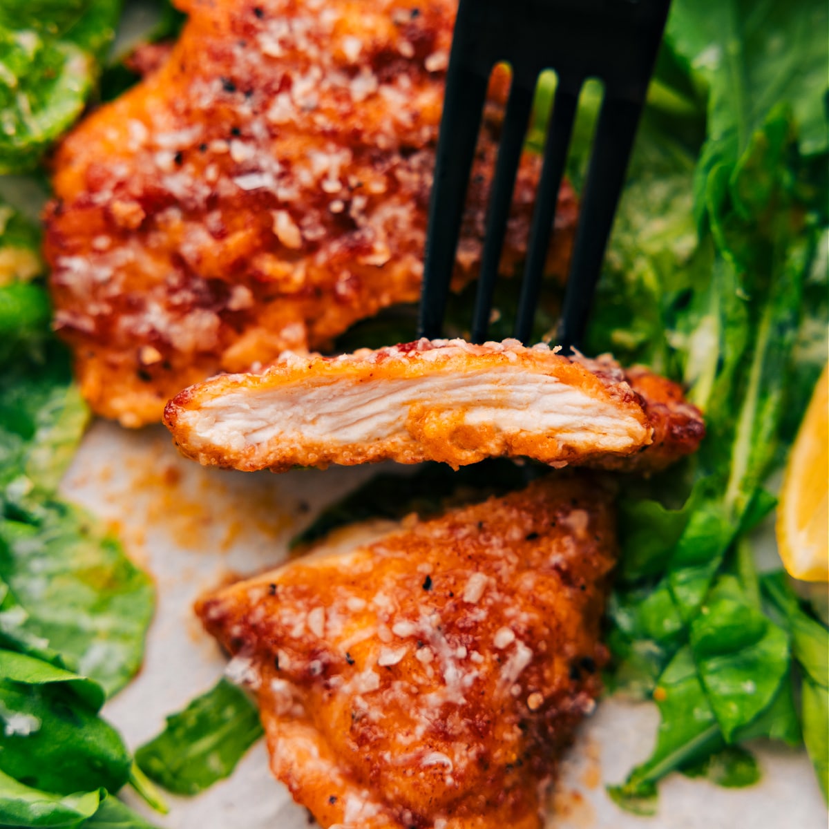 A slice of the chicken cutlet is held up with a spoon, showing its tender and perfectly cooked inside.