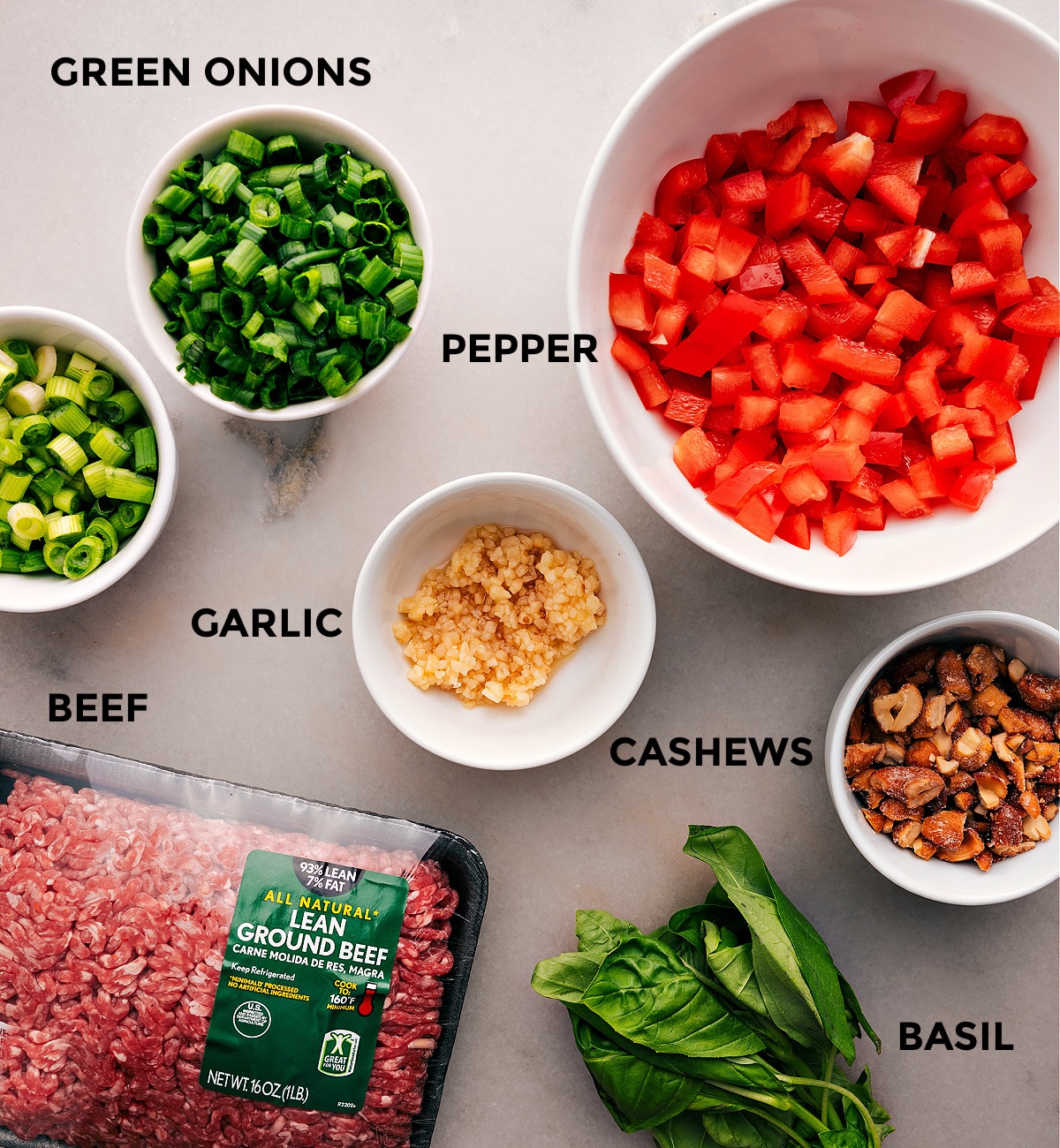 All the ingredients for this recipe are prepped and ready for easy assembly, including peppers, garlic, meat, cashews, and basil.