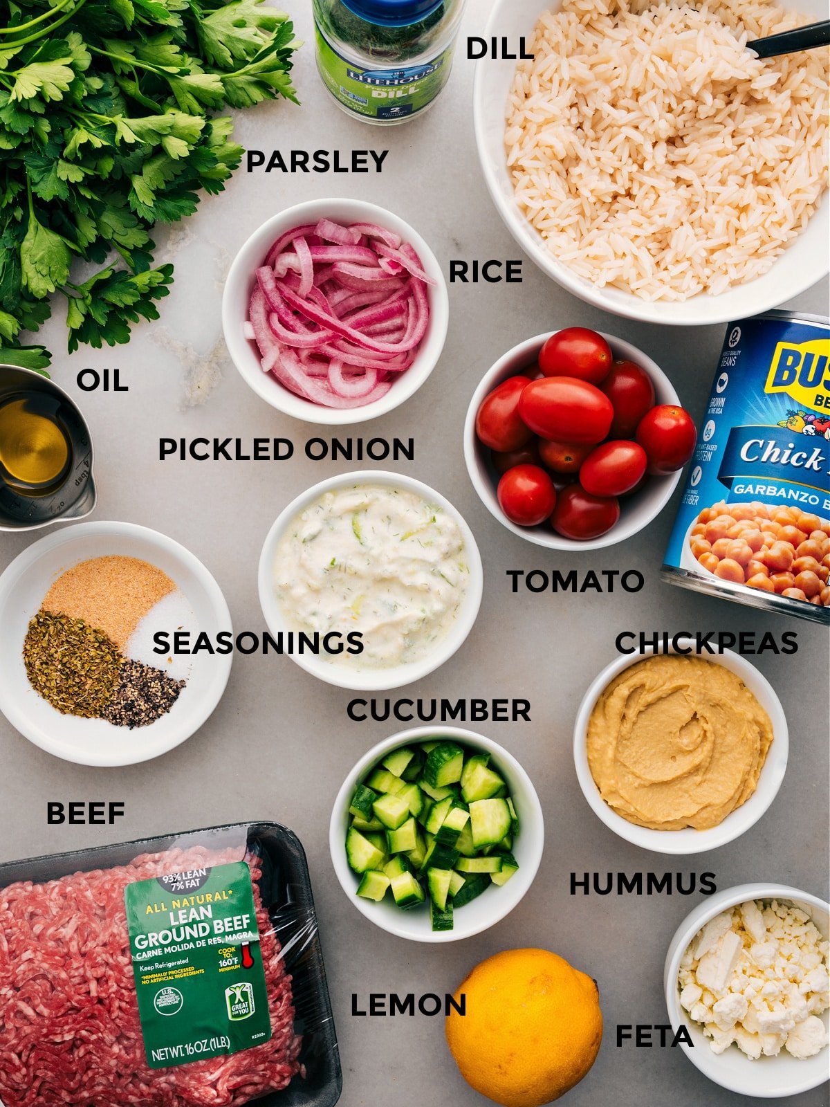 All the ingredients in this recipe are prepped for easy assembly: red onions, chickpeas, rice, veggies, seasonings, hummus, parsley, feta, lemon, and meat.