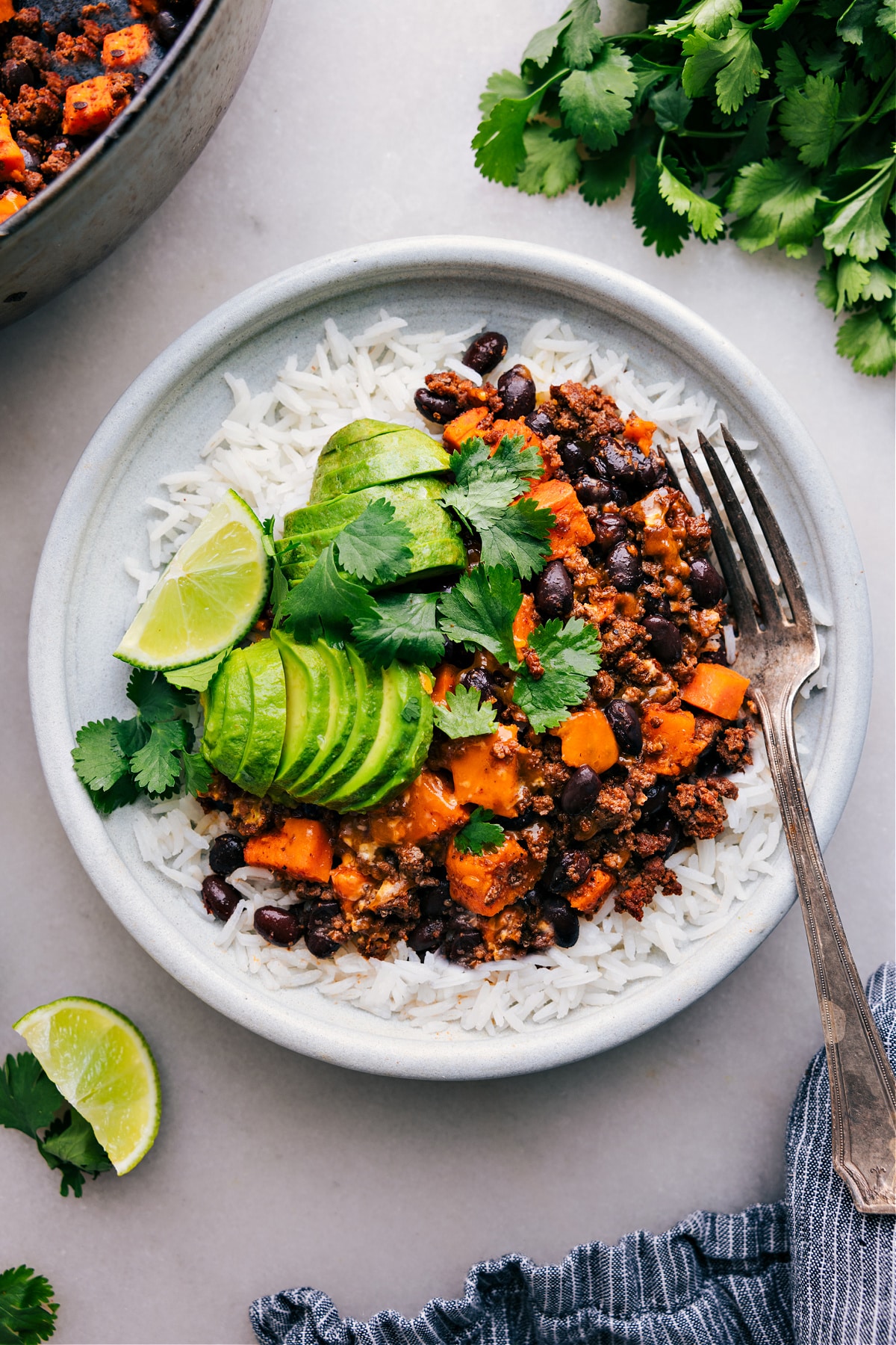 Ground Turkey Sweet Potato Skillet served on a plate of rice with fresh avocado, cilantro, and lime on the side.