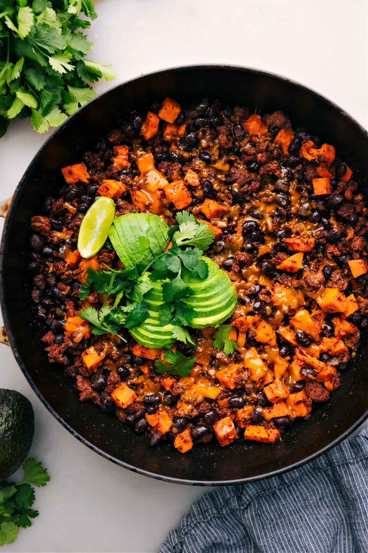 Ground Turkey Sweet Potato Skillet straight from the stove, topped with melty cheese, fresh avocado, and cilantro.