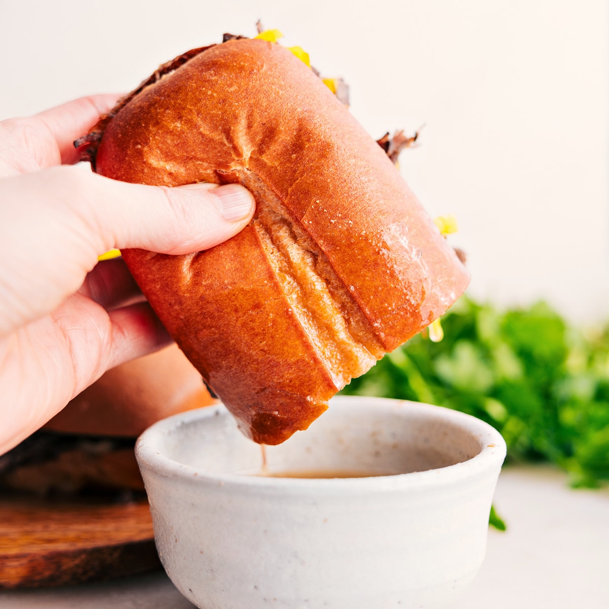 An Italian beef sandwich dipping into the broth from the crockpot.