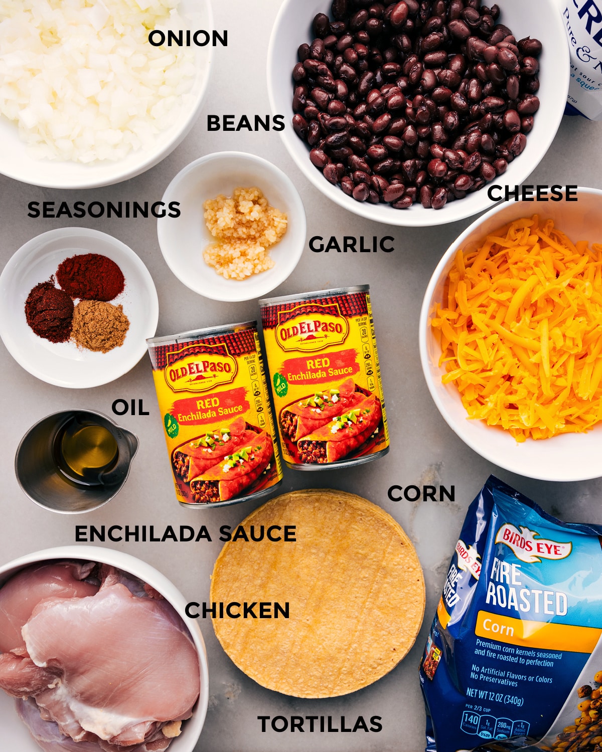 All the ingredients in this recipe—beans, sauce, cheese, tortillas, corn, seasonings, veggies, and meat—are prepped for easy assembly.